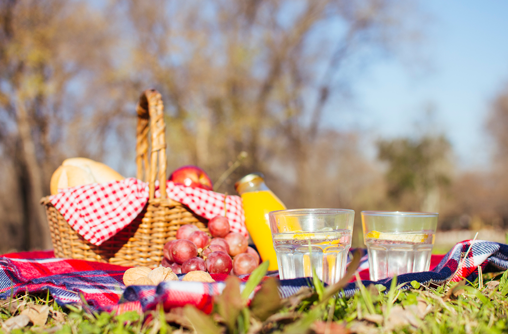 Picnic basket with food and drinks outside on picnic blanket