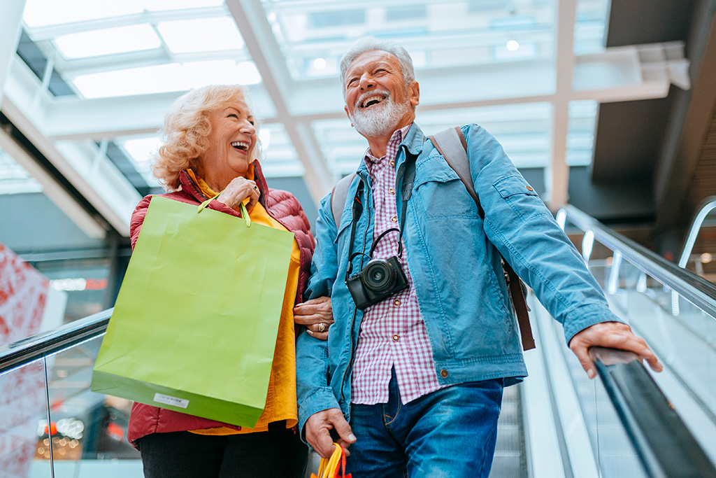 Elderly man and woman with shopping bags on an escalator.
