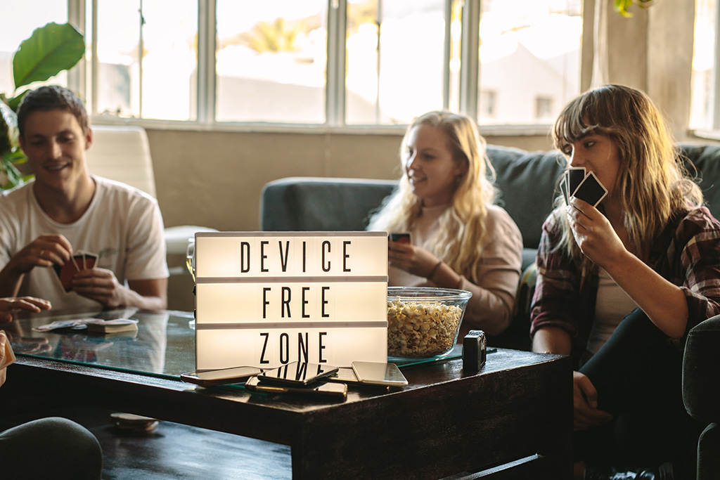 Group of friends playing card game with device free zone sign.