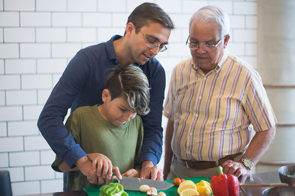 Grandfather, dad and son in kitchen cutting vegetables