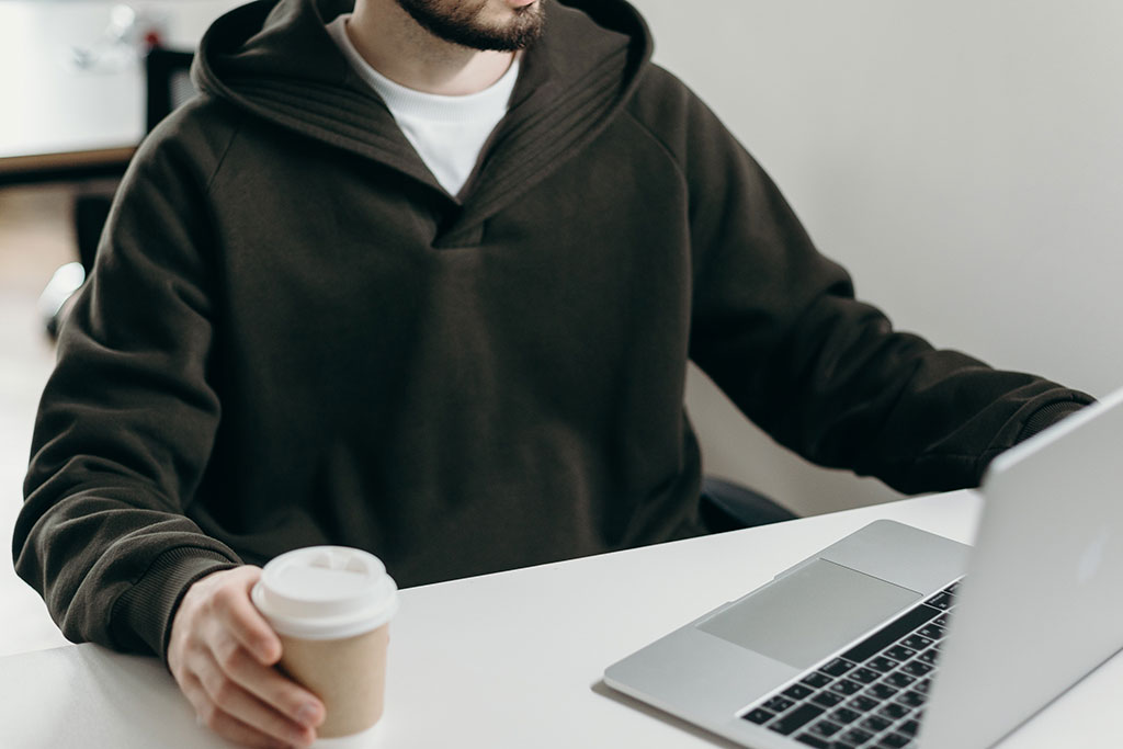 Man looking at laptop, holding coffee