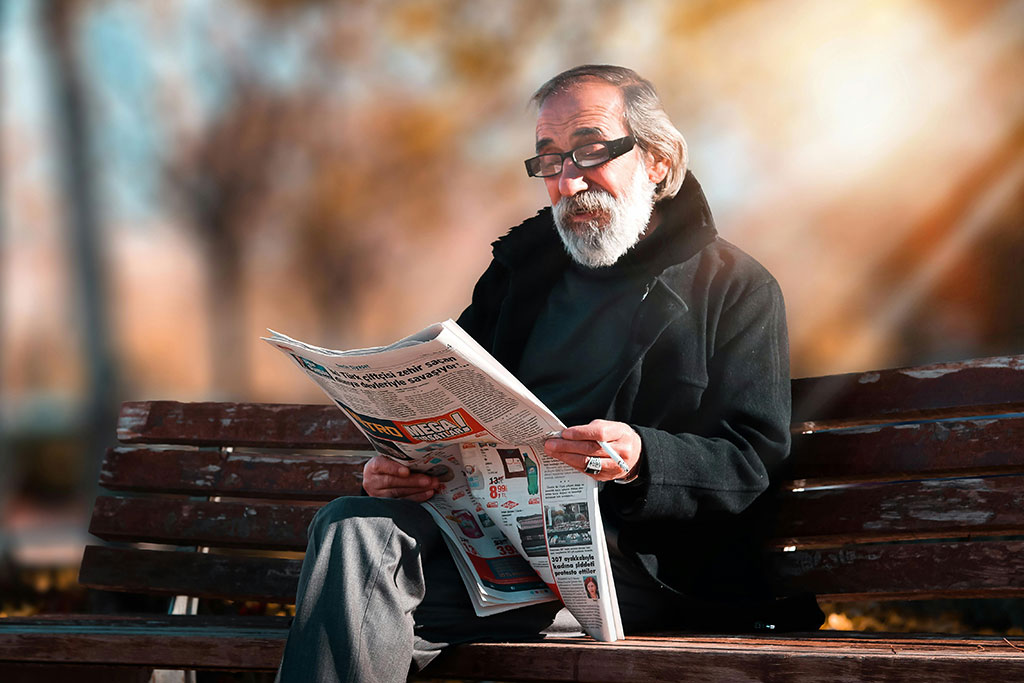 Older man on bench reading newspaper
