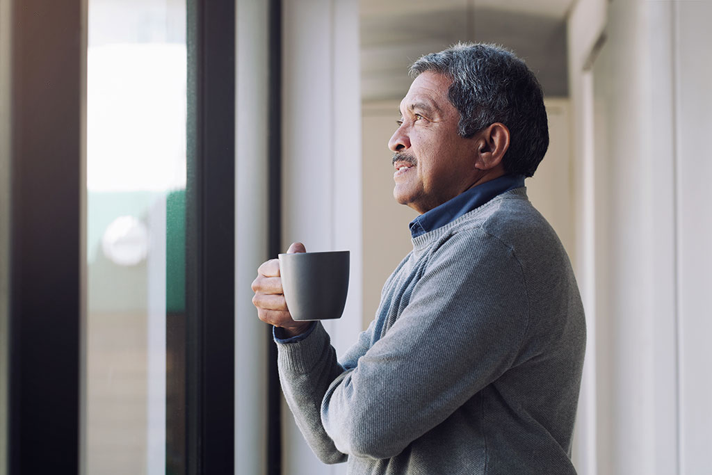 Man looking outside window with cup of coffee