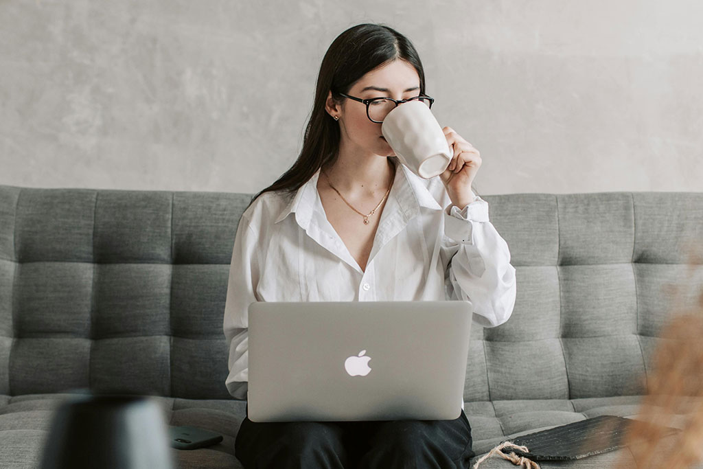 Young woman using laptop drinking coffee