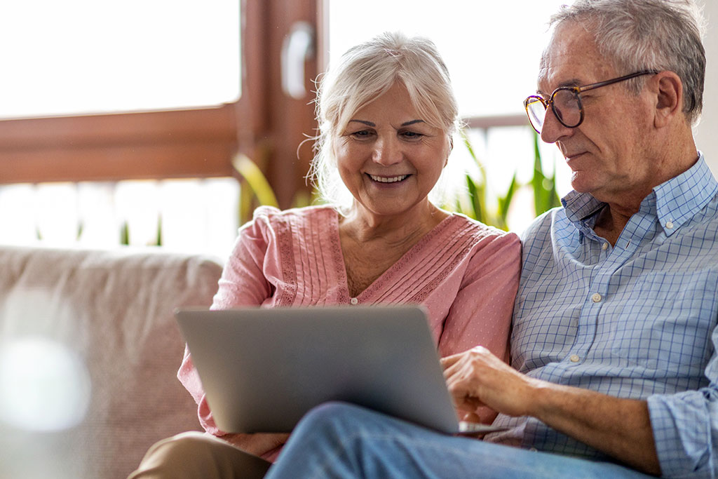 Older happy couple sitting on couch on tablet