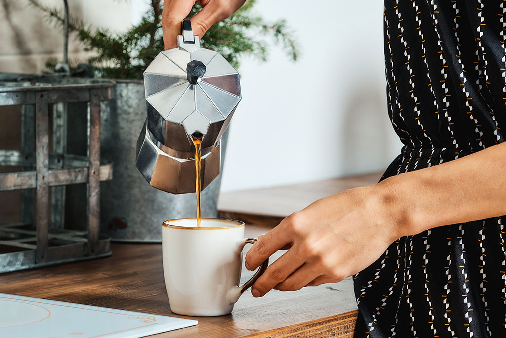 Person pouring espresso into coffee cup