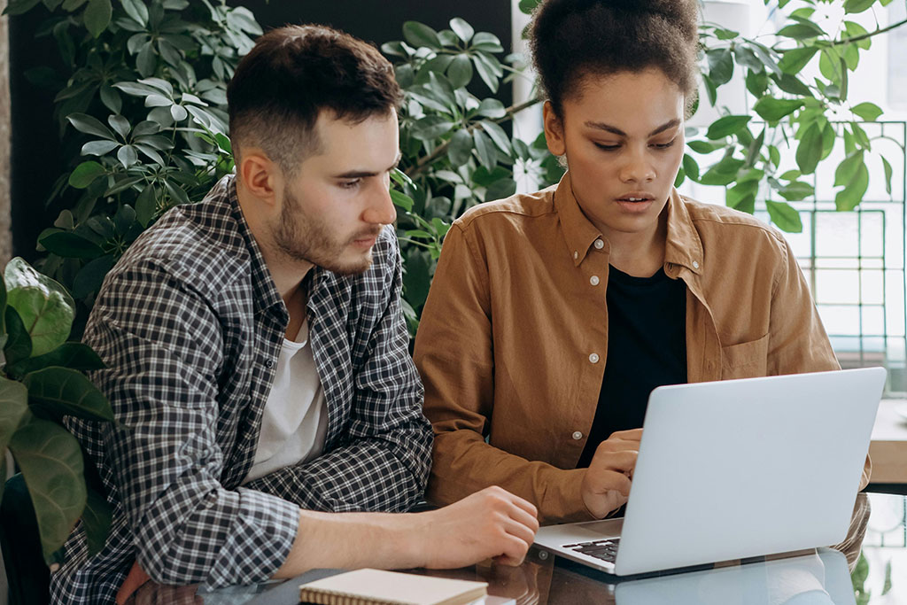 Couple sitting at table looking at laptop